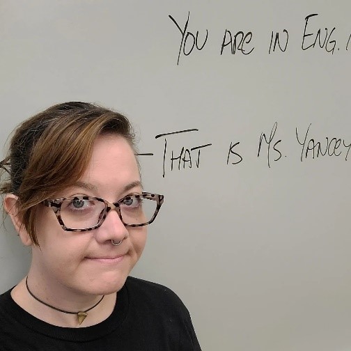 Image of me in front of dry erase board with writing that says, "You are in English 101. That is Ms. Yancey" and an arrow pointing toward me.